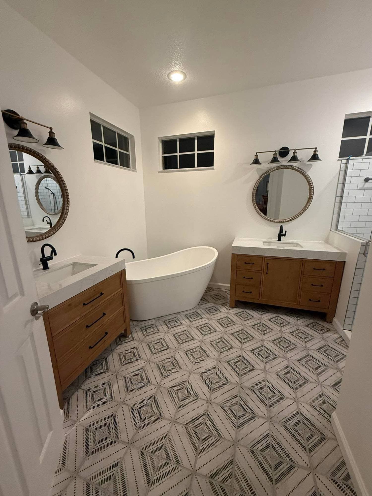 Bathroom makeover by I&I Home Repair, after: wood vanities, round mirrors, and a patterned tile floor